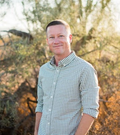 Phil is standing by himself in the Arizona desert. He is relaxed and smiling at the camera.